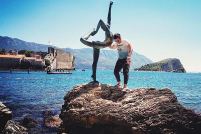 Men standing on rock by sea against sky