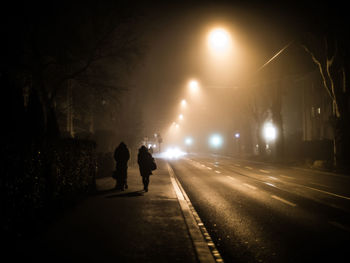 Silhouette people walking on illuminated sidewalk at night