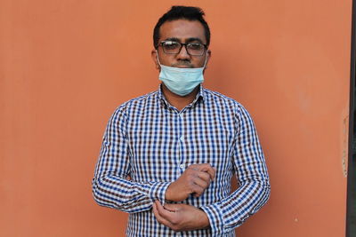 Portrait of young man closing cuff  standing against orange wall