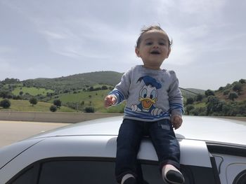 Boy standing on car against sky