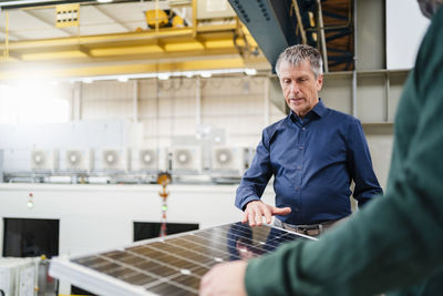 Businessman explaining solar panel to manager at factory