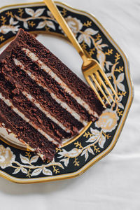Devil's food chocolate layer cake on black white gold plate with gold fork