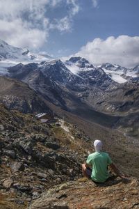 Rear view of woman sitting on snowcapped mountains against sky