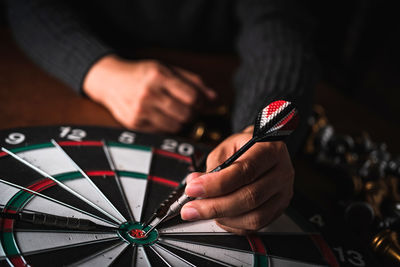 Midsection of person holding dart on dartboard