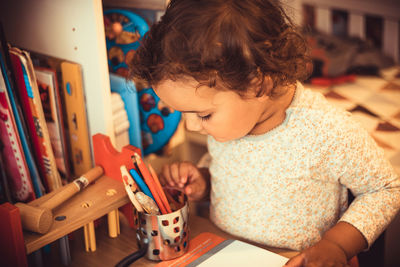 Little girl choosing crayons while coloring at home.