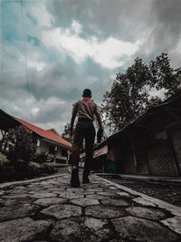 Rear view of man standing by house against sky