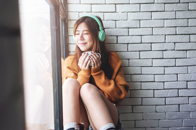 Smiling woman having drink while siting by window at home