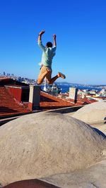 Full length of young man over rooftop against clear blue sky