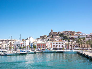 Sailboats in canal amidst buildings against clear blue sky