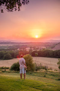 Rear view of man looking at landscape while standing on land against sky during sunset