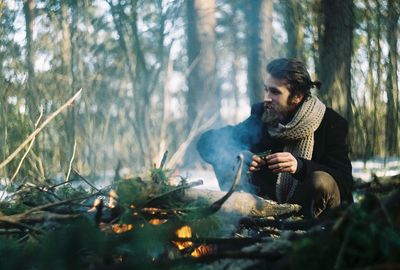 Man crouching by campfire in forest