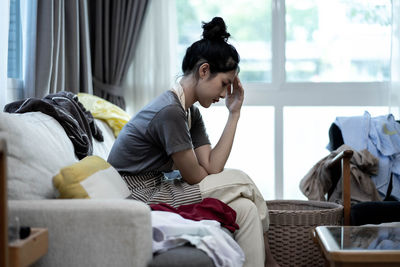 Side view of woman using phone while sitting on sofa at home