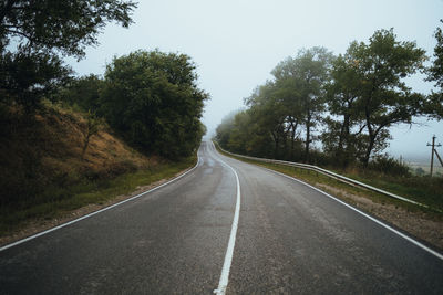 Road amidst trees against foggy sky