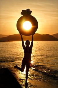 Silhouette woman standing on beach against sky during sunset