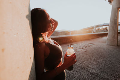 Woman with bottle standing against wall