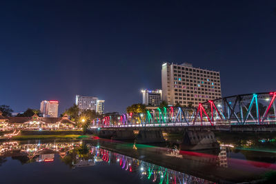 Illuminated modern buildings by river against sky at night