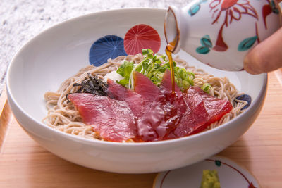 Close-up of hand holding food in bowl on table