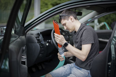 A young caucasian guy holds a tube with a nozzle in his hands and vacuums the seat in the car