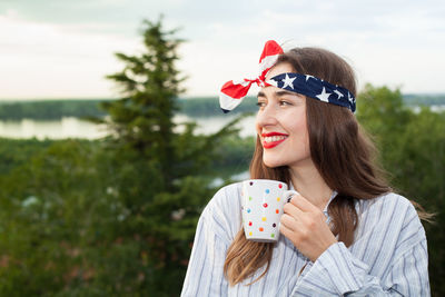 Smiling woman holding coffee cup while looking at view in forest