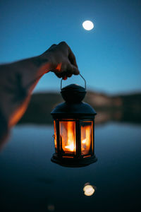Close-up of hand holding illuminated lamp against sky at night