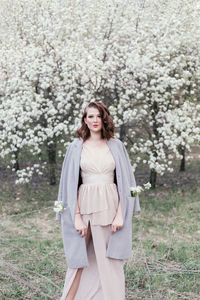 Portrait of a beautiful young woman standing by flower tree