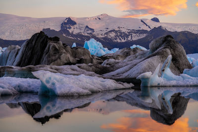 Scenic view of icebergs in sea against snowcapped mountains and sky during sunset