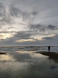 Silhouette man standing on beach against sky during sunset