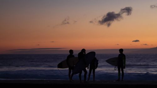 Silhouette people on beach against sky during sunset