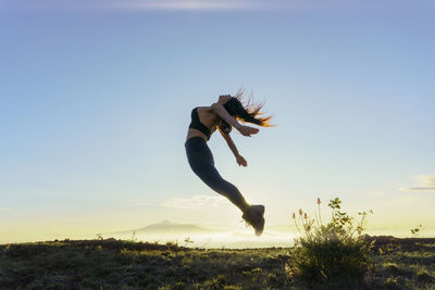 Low angle view of woman jumping against sky during sunset