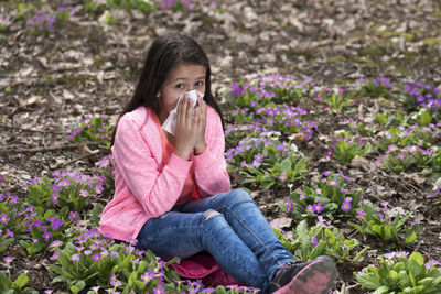 Portrait of girl cleaning nose while sitting on flowering plants