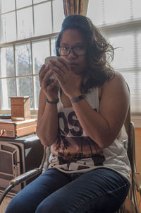 Portrait of young woman sitting on chair by window