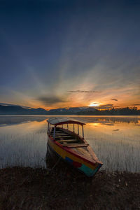 Boat moored on beach against sky during sunset