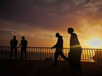 Silhouette people standing by railing against sky during sunset