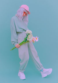 Full length portrait of woman with flowers while standing over blue background