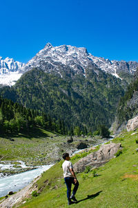 Rear view of man walking on snowcapped mountains against clear blue sky