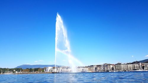 Fountain in city against clear blue sky