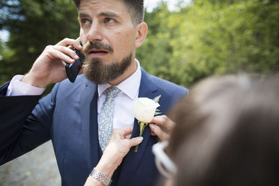Cropped image of woman adjusting boutonniere on bridegroom's jacket at wedding ceremony