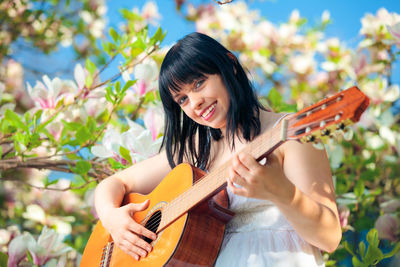 Portrait of smiling young woman playing guitar in park