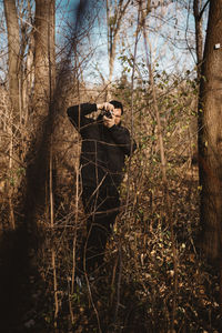 Man standing by tree trunk in forest