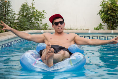 Portrait of shirtless young man relaxing on pool raft in swimming pool