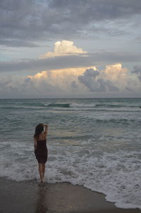 Rear view of woman standing at beach during sunset