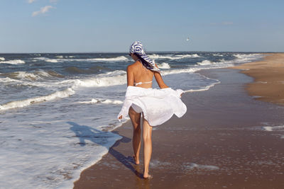 Woman run in a white bathing suit and hat sunglasses on an empty sandy beach