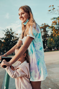 Teenager girl and her sister preschooler riding an electric scooter in the city center