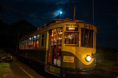 Train on illuminated street against sky at night