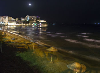 Illuminated city by sea against sky at night