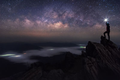 Man with illuminated light on cliff against star field