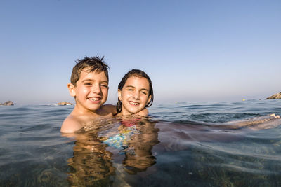 Portrait of siblings swimming in sea against clear sky