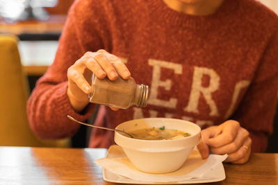 Woman adds black pepper to fish soup with salmon at seafood restaurant. female hand shake pepperbox.