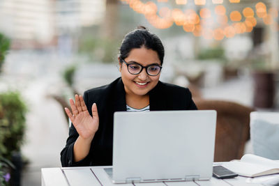 A young indian woman is holding a video conference sitting in a cafe on the terrace. freelance