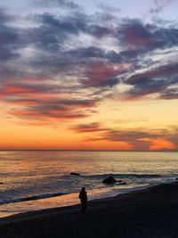 Silhouette people looking at sea against sky during sunset